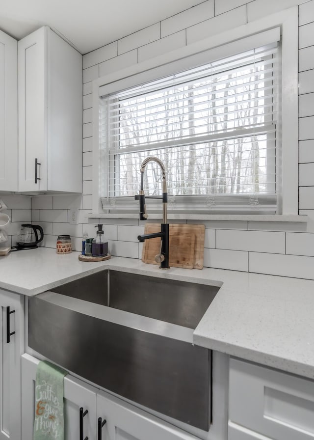 kitchen with light stone countertops, tasteful backsplash, white cabinets, and a sink