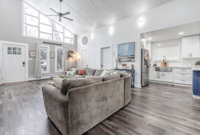 living area featuring high vaulted ceiling, baseboard heating, wood finished floors, and a ceiling fan