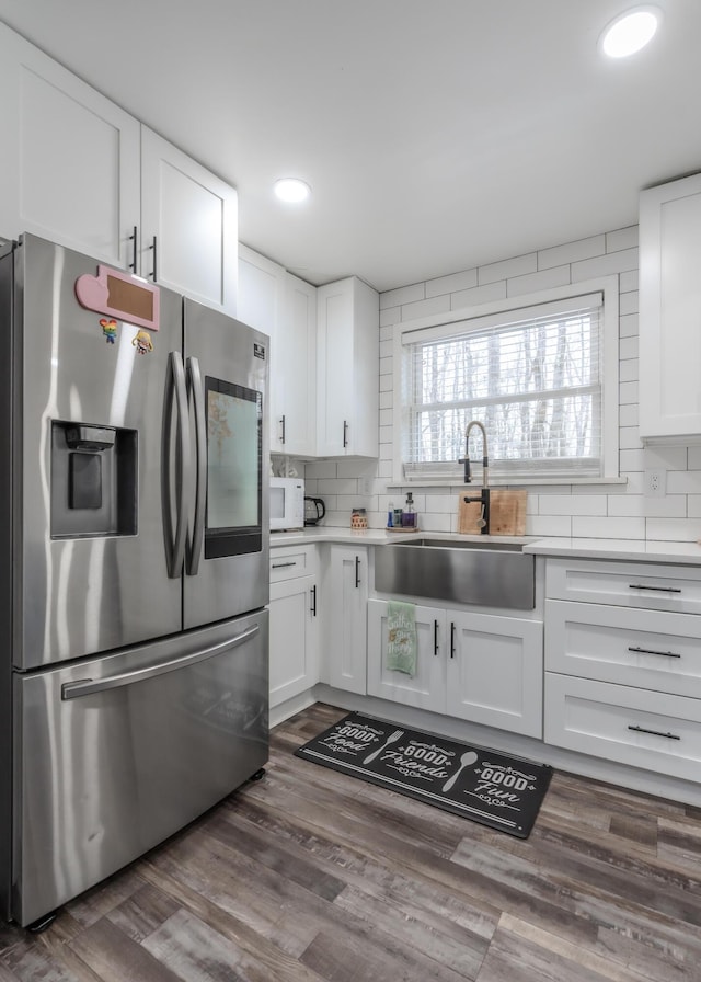 kitchen featuring white cabinets, decorative backsplash, stainless steel fridge with ice dispenser, white microwave, and a sink