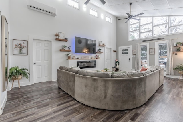 living room with a glass covered fireplace, dark wood finished floors, a wall unit AC, and ceiling fan