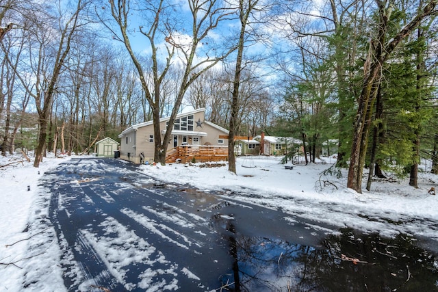 snow covered property with a shed, a detached garage, and an outbuilding