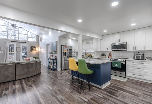 kitchen featuring a kitchen island, appliances with stainless steel finishes, open floor plan, a breakfast bar area, and light countertops