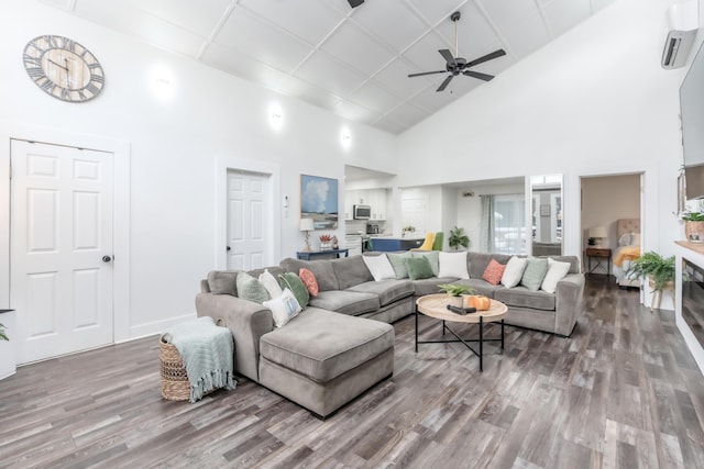 living area with a towering ceiling, a wall mounted AC, a ceiling fan, wood finished floors, and baseboards