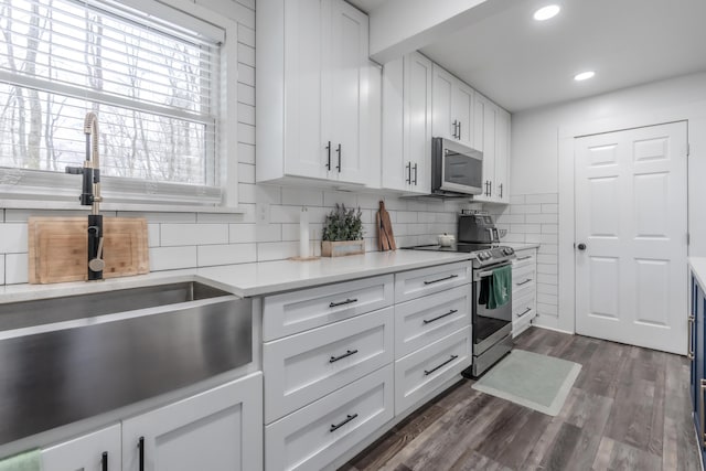 kitchen featuring white cabinets, light countertops, appliances with stainless steel finishes, dark wood-style floors, and tasteful backsplash