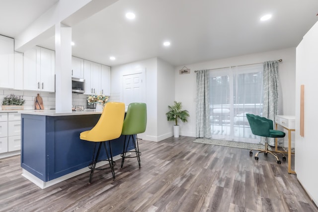 kitchen featuring light countertops, stainless steel microwave, backsplash, white cabinetry, and wood finished floors