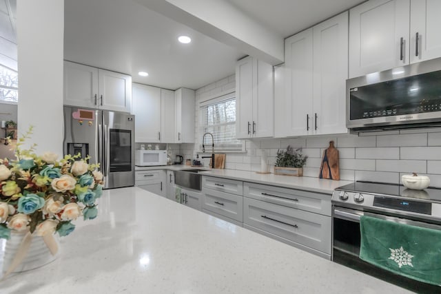 kitchen featuring stainless steel appliances, tasteful backsplash, white cabinets, a sink, and light stone countertops