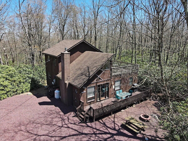 exterior space featuring a shingled roof, a wooden deck, and a chimney