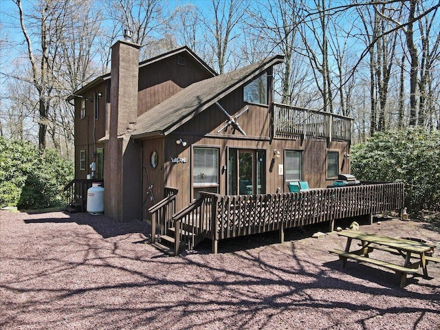 back of house with a shingled roof, a chimney, and a deck
