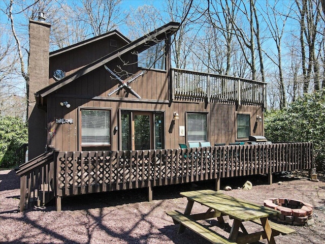 back of house with an outdoor fire pit, a wooden deck, and a chimney