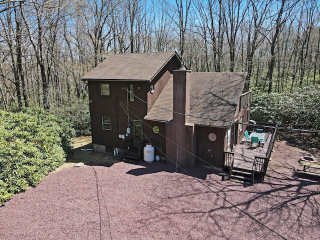 view of side of home with a wooden deck and roof with shingles