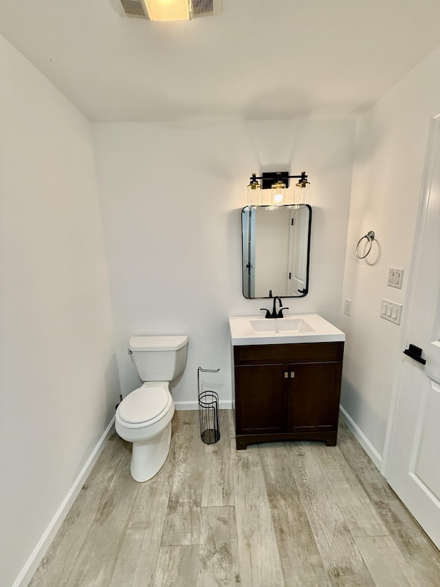 half bathroom with toilet, baseboards, wood finished floors, and vanity