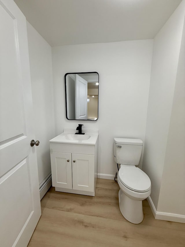 bathroom featuring baseboards, toilet, wood finished floors, baseboard heating, and vanity