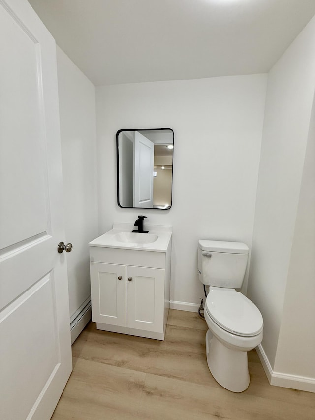 half bath with a baseboard radiator, toilet, vanity, wood finished floors, and baseboards