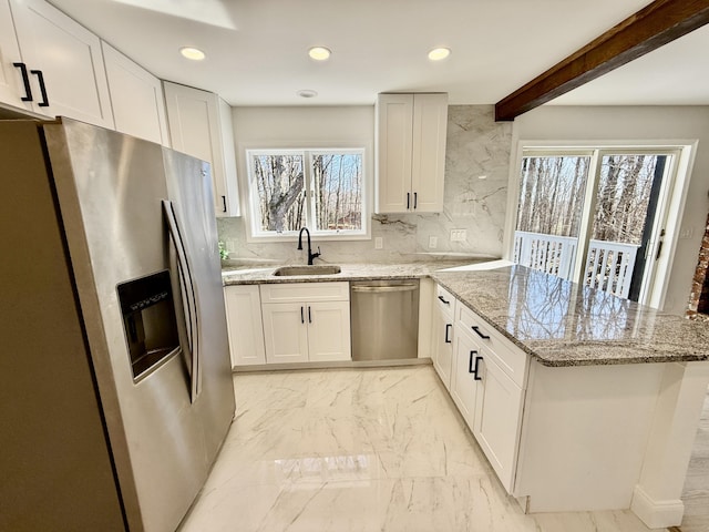 kitchen with appliances with stainless steel finishes, a peninsula, marble finish floor, white cabinetry, and a sink