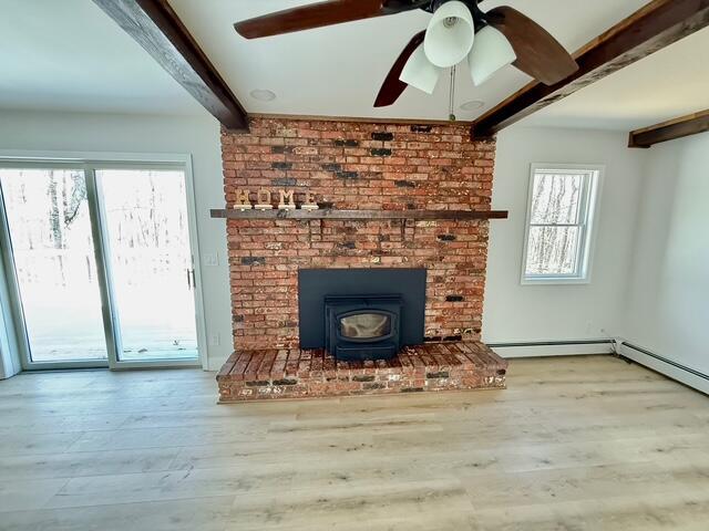 unfurnished living room featuring a baseboard radiator, a ceiling fan, a wood stove, wood finished floors, and beamed ceiling