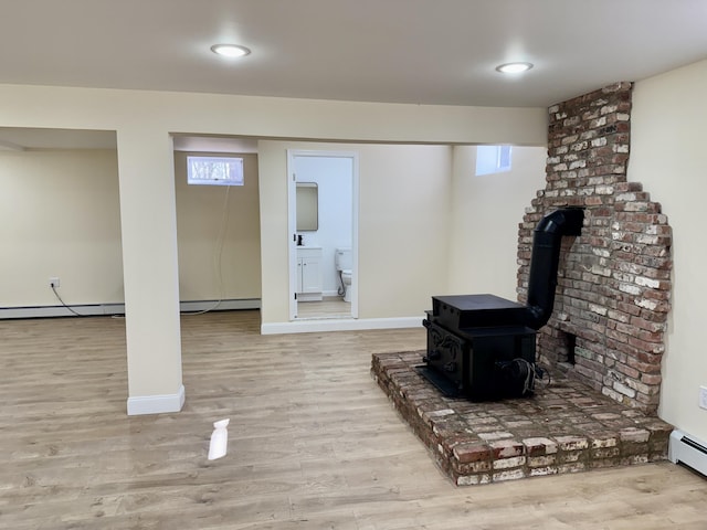 basement featuring baseboard heating, wood finished floors, a wood stove, and baseboards