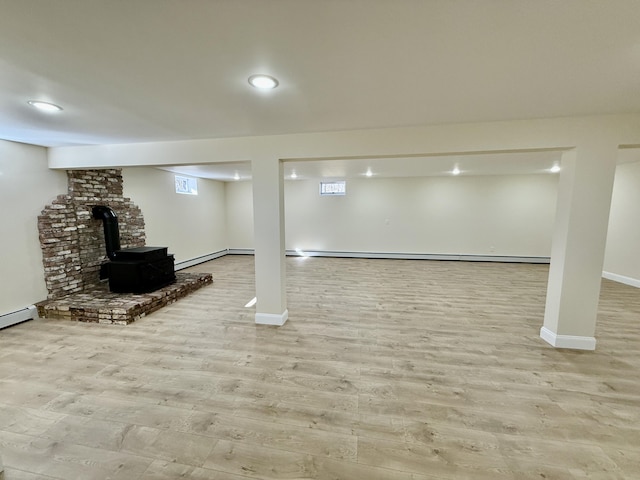 finished basement with a wood stove, a baseboard radiator, baseboards, and wood finished floors