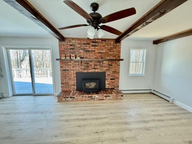 unfurnished living room with a wood stove, beamed ceiling, baseboards, and wood finished floors