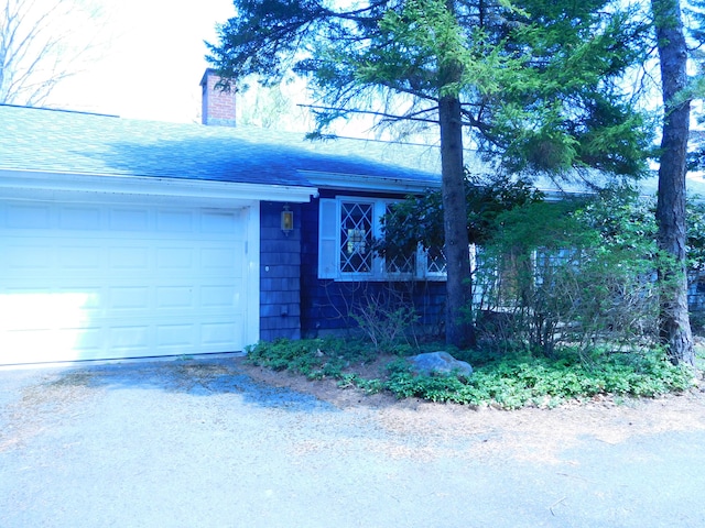 single story home featuring roof with shingles, a chimney, driveway, and a garage