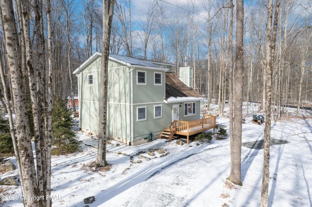 snow covered house featuring a chimney, a deck, and a shingled roof