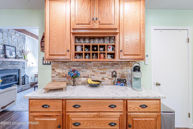 kitchen featuring light stone counters, backsplash, a fireplace, and dark wood-style flooring