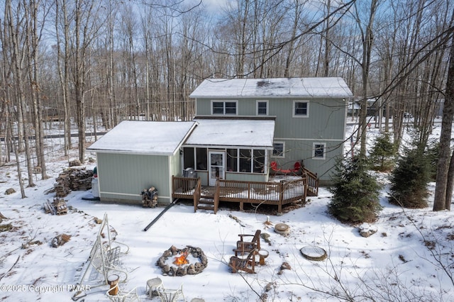 snow covered back of property featuring a deck, a fire pit, and a sunroom