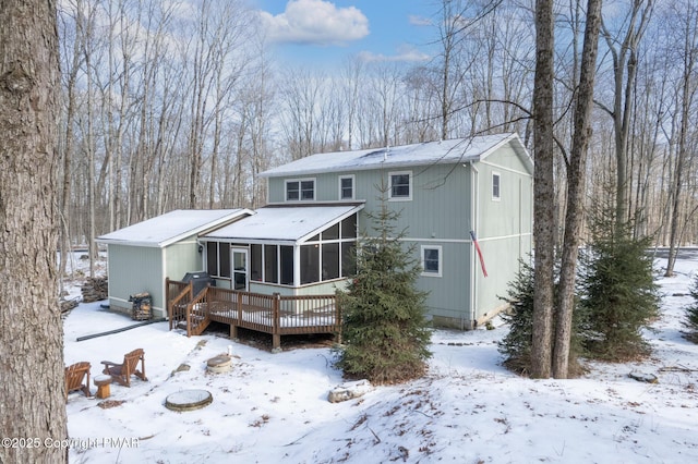 snow covered back of property with a deck and a sunroom