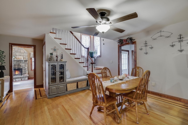 dining room with light wood-style floors, ceiling fan, stairway, and a fireplace