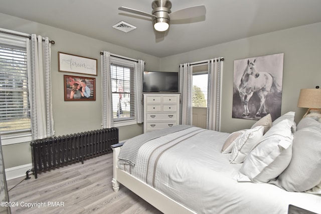 bedroom featuring ceiling fan, visible vents, baseboards, radiator, and light wood finished floors