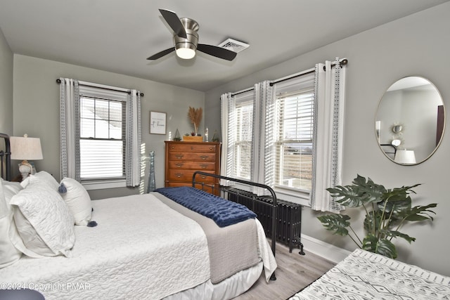 bedroom with baseboards, multiple windows, visible vents, and wood finished floors