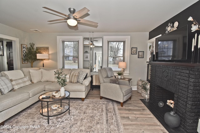 living area with a brick fireplace, visible vents, ceiling fan, and wood finished floors