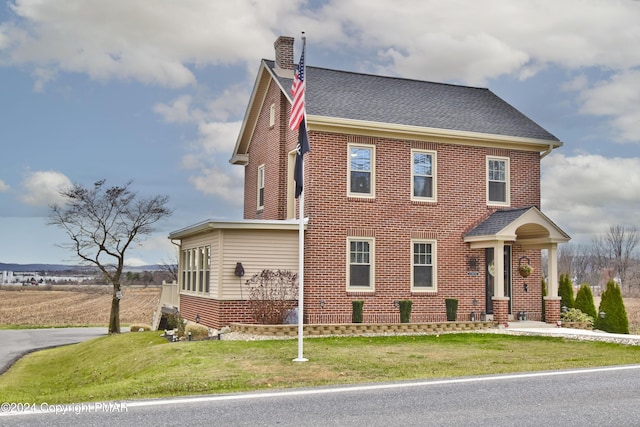 view of front of house with roof with shingles, a front lawn, and a chimney