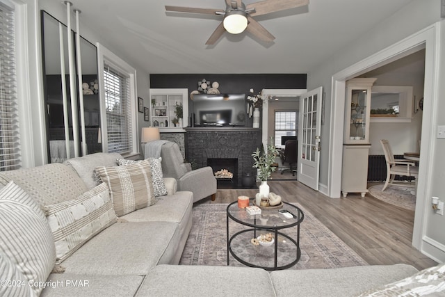 living area with a brick fireplace, wood finished floors, a ceiling fan, and baseboards