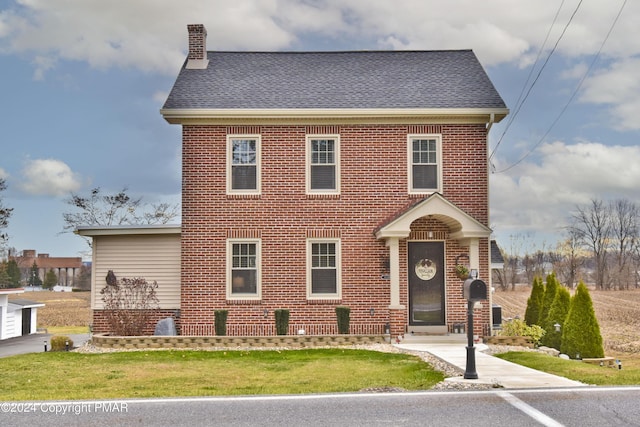 view of front facade featuring brick siding, a chimney, and a front yard