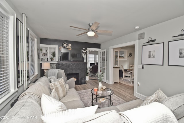 living area with wood finished floors, visible vents, a ceiling fan, baseboards, and a brick fireplace