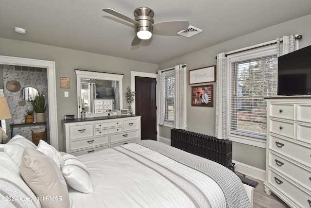 bedroom with radiator, visible vents, ceiling fan, wood finished floors, and baseboards