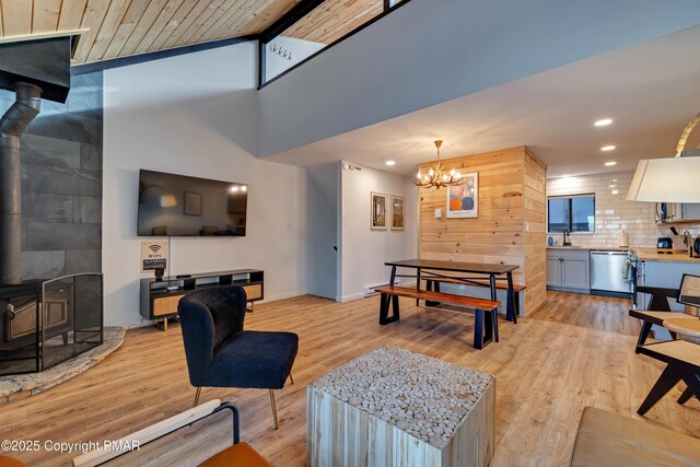 living room with lofted ceiling, a wood stove, sink, a notable chandelier, and light hardwood / wood-style flooring