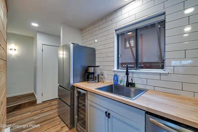 kitchen featuring appliances with stainless steel finishes, wood counters, sink, wine cooler, and light hardwood / wood-style flooring