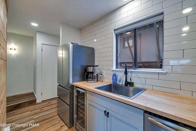 kitchen with beverage cooler, butcher block countertops, appliances with stainless steel finishes, light wood-type flooring, and a sink