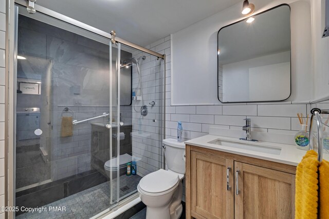 bathroom featuring vanity, a shower with shower door, tile walls, and toilet