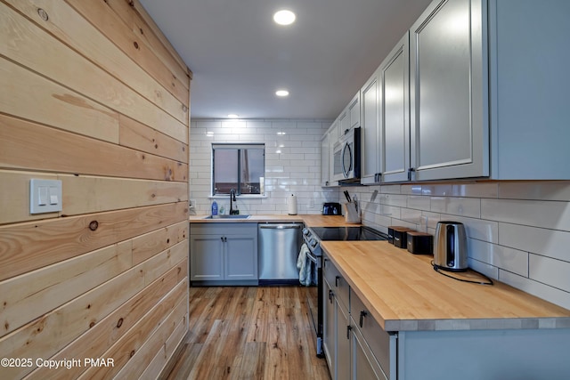 kitchen with stainless steel appliances, tasteful backsplash, light wood-style floors, a sink, and butcher block countertops