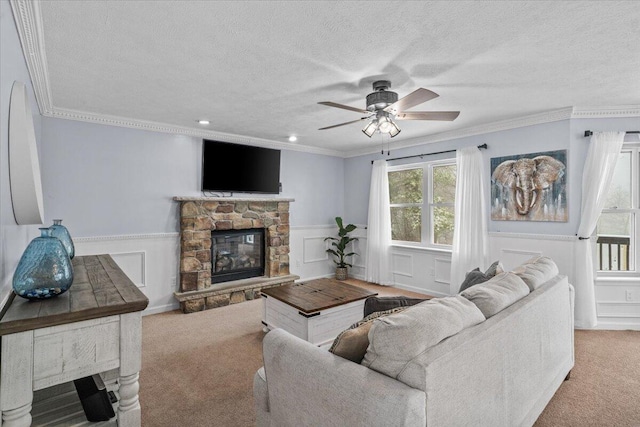living area with a ceiling fan, a fireplace, crown molding, wainscoting, and carpet flooring