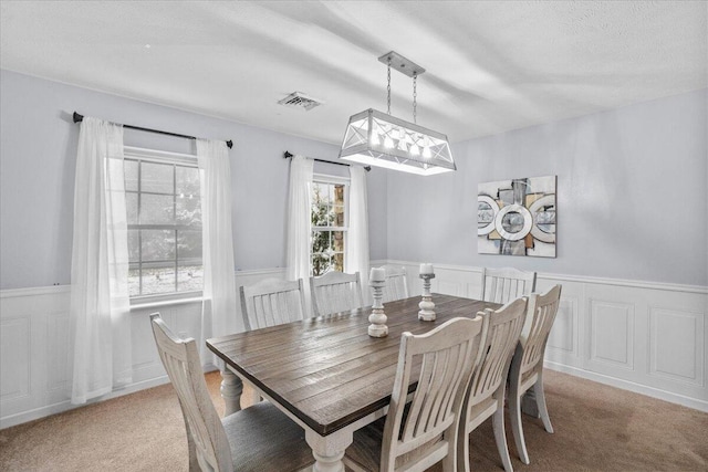 carpeted dining area featuring visible vents and wainscoting