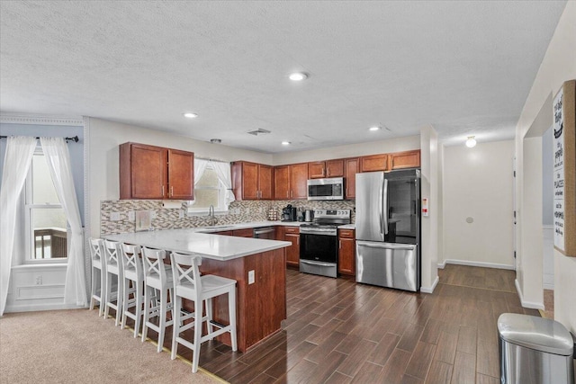kitchen featuring brown cabinetry, a peninsula, tasteful backsplash, appliances with stainless steel finishes, and a sink