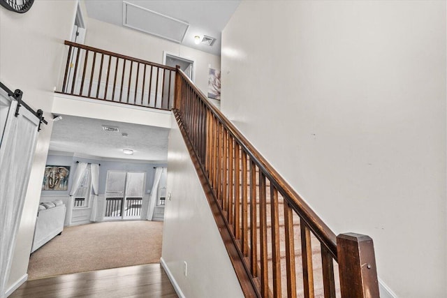 stairway featuring visible vents, baseboards, a barn door, and wood finished floors