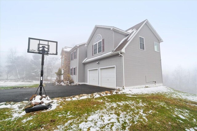 snow covered property with aphalt driveway and a garage