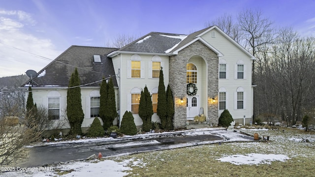 traditional-style home featuring entry steps, stone siding, and roof with shingles