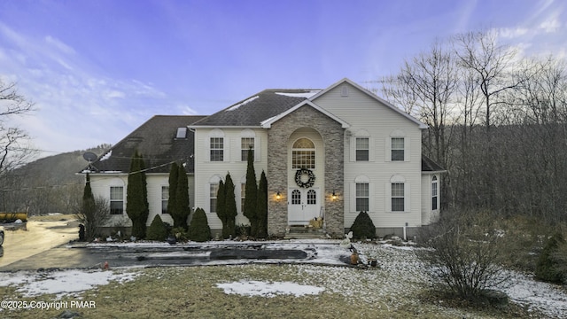 view of front of property with entry steps, stone siding, and roof with shingles