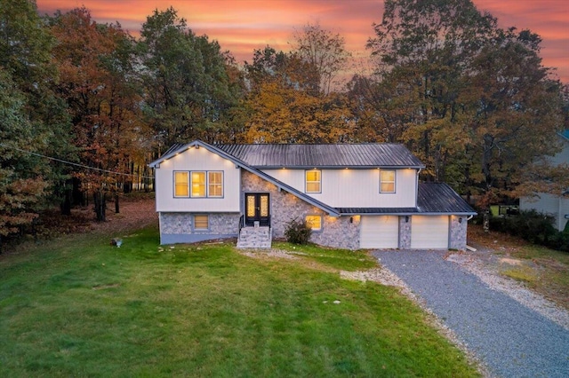 view of front of property featuring stone siding, driveway, metal roof, and a yard