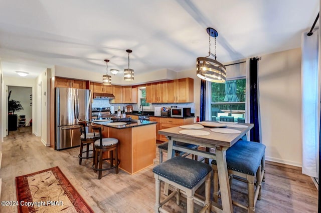 kitchen featuring a center island, dark countertops, appliances with stainless steel finishes, light wood-type flooring, and under cabinet range hood